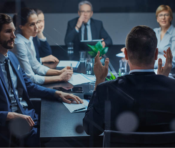 Late at Night In the Corporate Office Meeting Room: At Conference Table Executive Director Talks to a Board of Directors, Investors and Business Associates  Over the Shoulder Shot 